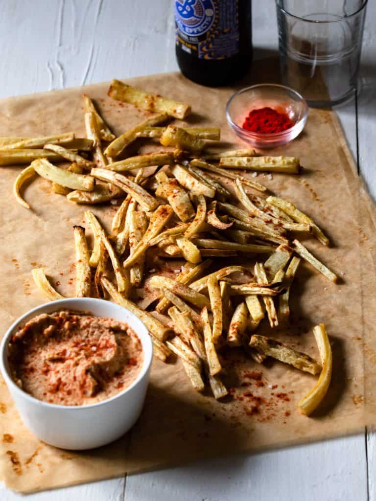 Parsnips baked in the oven served on parchment paper with a sun-dried tomato hummus.